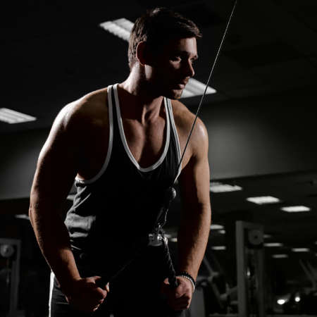 Muscular athletic young man fitness model do exercises in gym