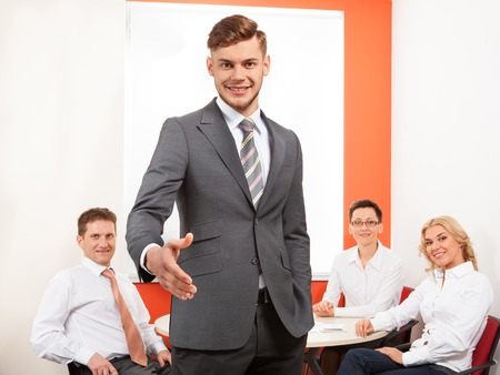 Portrait of happy businessman offering handshake and his team in office