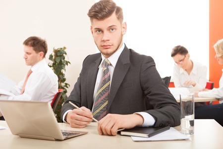 man working on laptop with colleagues in the backgroundの写真素材