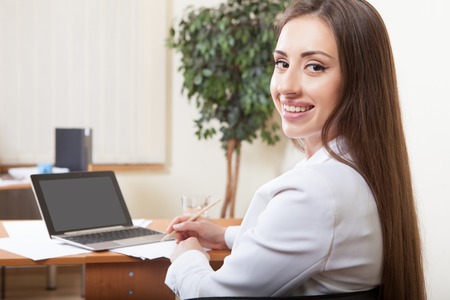 Portrait of happy brown hair woman using laptop in officeの写真素材