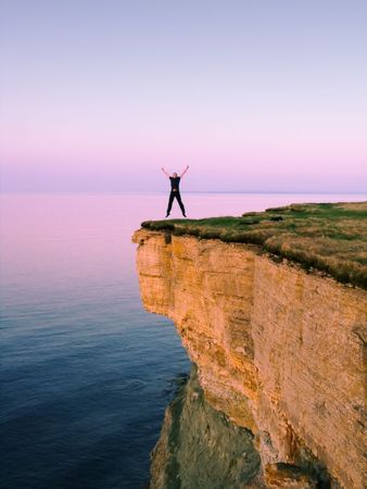 young man jumping on the cliff with spreaded handsの写真素材