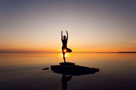 caucasian fitness woman practicing yoga on the beach at sunsetの写真素材