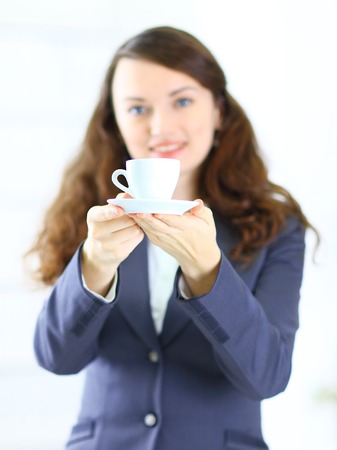 Business woman offers a cup of coffee in the officeの写真素材