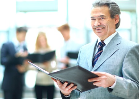 Successful business man standing with his staff in background at officeの写真素材