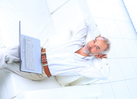 Senior man in sofa with laptop computerの写真素材