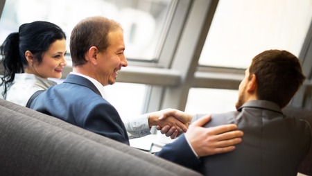 Mature businessman shaking hands to seal a deal with his partner and colleagues in a modern officeの写真素材