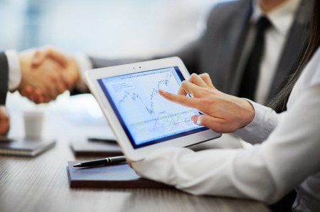 The tablet with the schedule in the foreground. Business partners shaking hands in office.