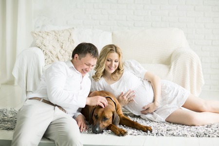 husband, pregnant wife and dog resting on the bed with the bedroomの写真素材