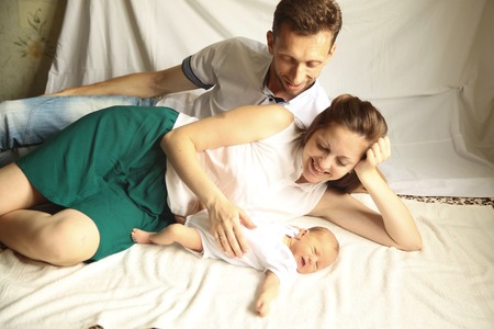 family happiness concept - happy mother and father lie side by a newborn baby