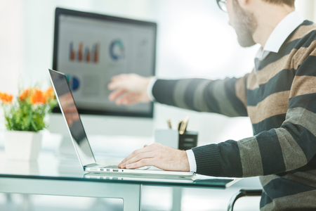 Finance specialist working on laptop with financial charts and marketing schemes in the modern officeの写真素材