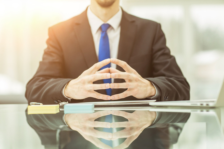 concept of business success:successful businessman sitting behind a Desk, hands folded in front of him.の写真素材