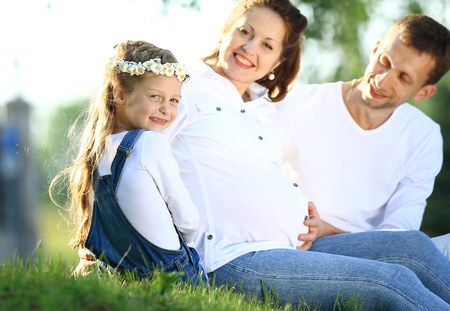 expectant parents and their little daughter sitting on the grassの写真素材