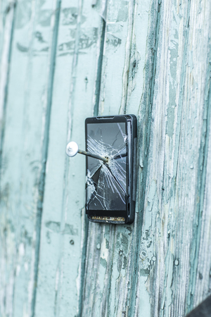 concept of obsolete technology:mobile phone nailed to the fence a large nailの写真素材