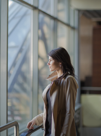Confident business woman stands near a large office windowの写真素材