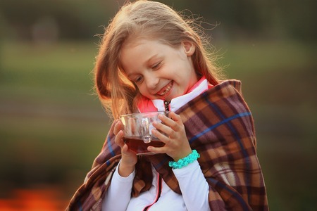 little girl with a Cup of hot cocoa wrapped in a blanket sittingの写真素材