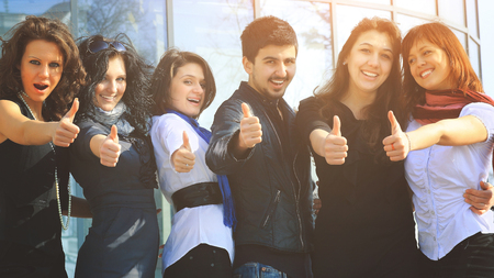 group of college students smiling friendly standing next to each other with arms extended forward and the thumbs upの写真素材