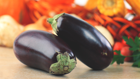 Eggplant in the foreground. Composition with raw vegetables and wicker basketの写真素材