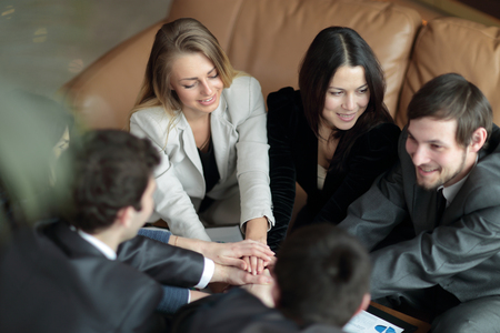 Group of happy business people holding hands together while sitting around the deskの写真素材