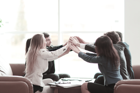 Group of happy business people holding hands together while sitting around the deskの写真素材