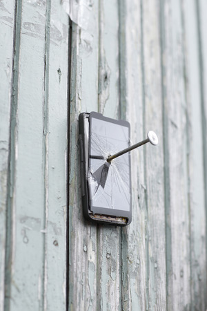 faulty mobile phone is nailed to an old fence.the concept of obsolete technologyの写真素材