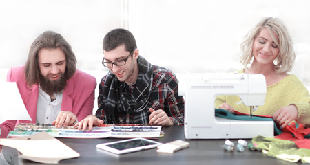 Smiling tailor businesswoman sitting at sewing machine and making handmade clothing while marketing assistant working on new projecの写真素材