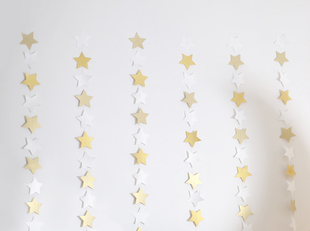 Christmas lights gold stars are burning on the white wall.の写真素材