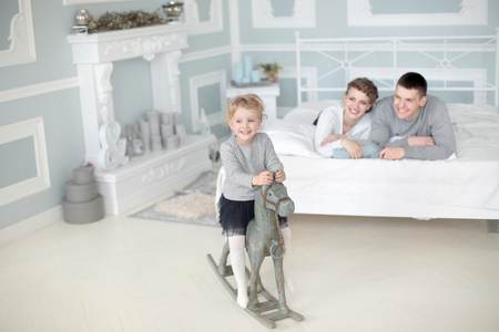 Happy family of three sit in room and play with daughter on her wooden toy horseの写真素材