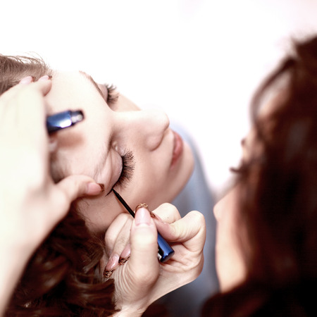Beautiful woman with makeup brush near her face on a white background.