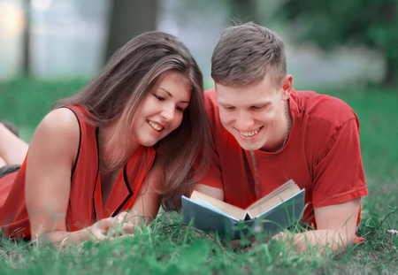 couple of students lying on the grass in the Park and reading a bookの写真素材