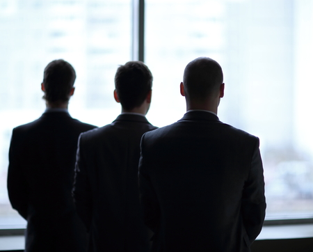 rear view of three businessmen as they stare at the big window overlooking the cityの写真素材