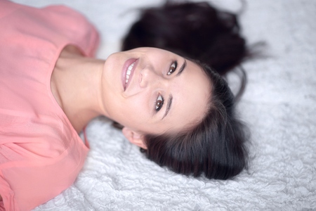 close up.thoughtful young woman lying on white carpet in living roomの写真素材
