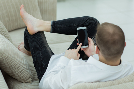rear view.young man looking through a text on his smartphoneの写真素材