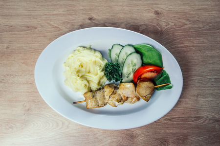 mashed potatoes and kebab on a wooden skewer in a white plate on a wooden backgroundの写真素材