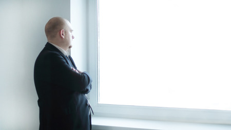 Pensive businessman looking at a blank office windowの写真素材