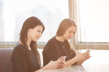 employees using their smartphones sitting at a table in a cafeの写真素材