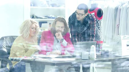 view from behind glass.three colleagues discussing new ideas in the Studioの写真素材