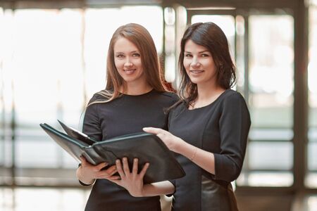 Two business women read business documents standing in the office lobby.の写真素材