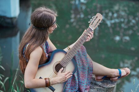 beautiful hippie girl playing guitar near forest lake
