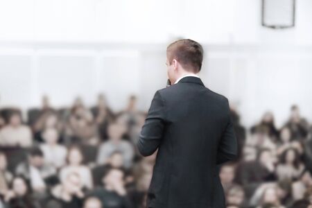 rear view.young businessman at a business conference with a public report.