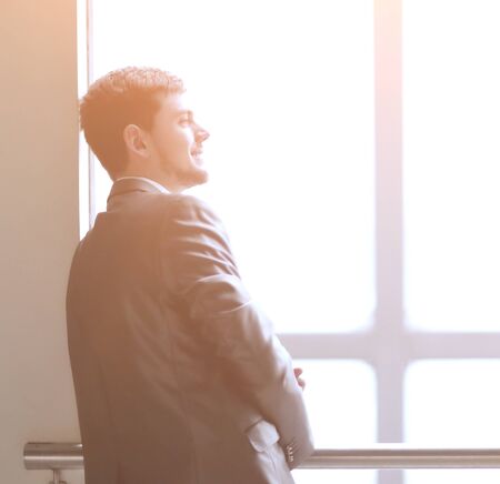 smiling businessman standing near a large office windowの写真素材