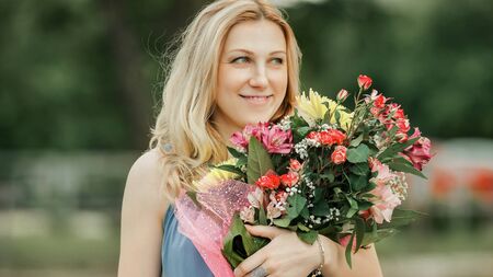 beautiful woman with a bouquet of flowers standing on the grass in the city Parkの写真素材