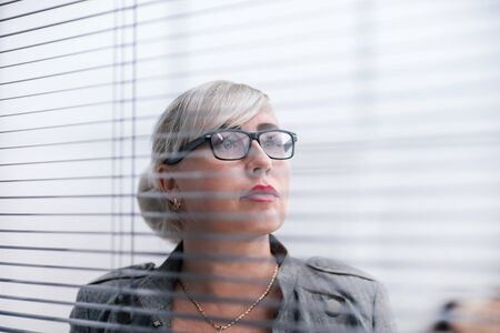 through the blinds. serious business woman standing in office.