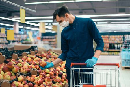 young man in a protective mask standing near the counter with apples. photo with a copy of the spaceの写真素材
