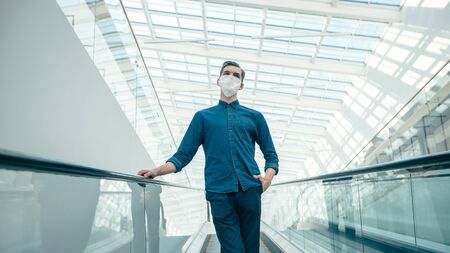 young man in a protective mask standing on the escalator steps.の写真素材