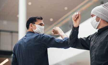 A young man in a protective mask while welcoming his friendの写真素材