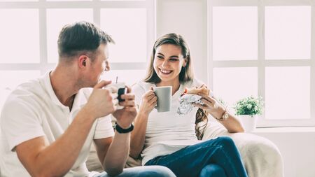 Young couple drinks coffee sitting on the sofa in a new apartment.の写真素材