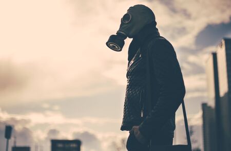 casual young man in a gas mask standing on the street in an empty cityの写真素材