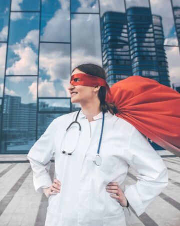 female doctor in a superhero raincoat looks at a city street .の写真素材