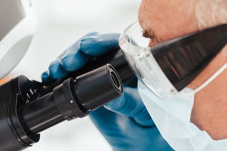 scientist biologist in a protective mask looking through a microscope.