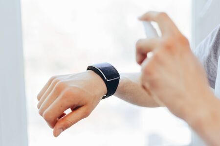 close up. young man is spraying alcohol antiseptic on his smart watch.の写真素材